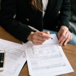 Close-up of a person reviewing and signing documents at a wooden desk, business attire.