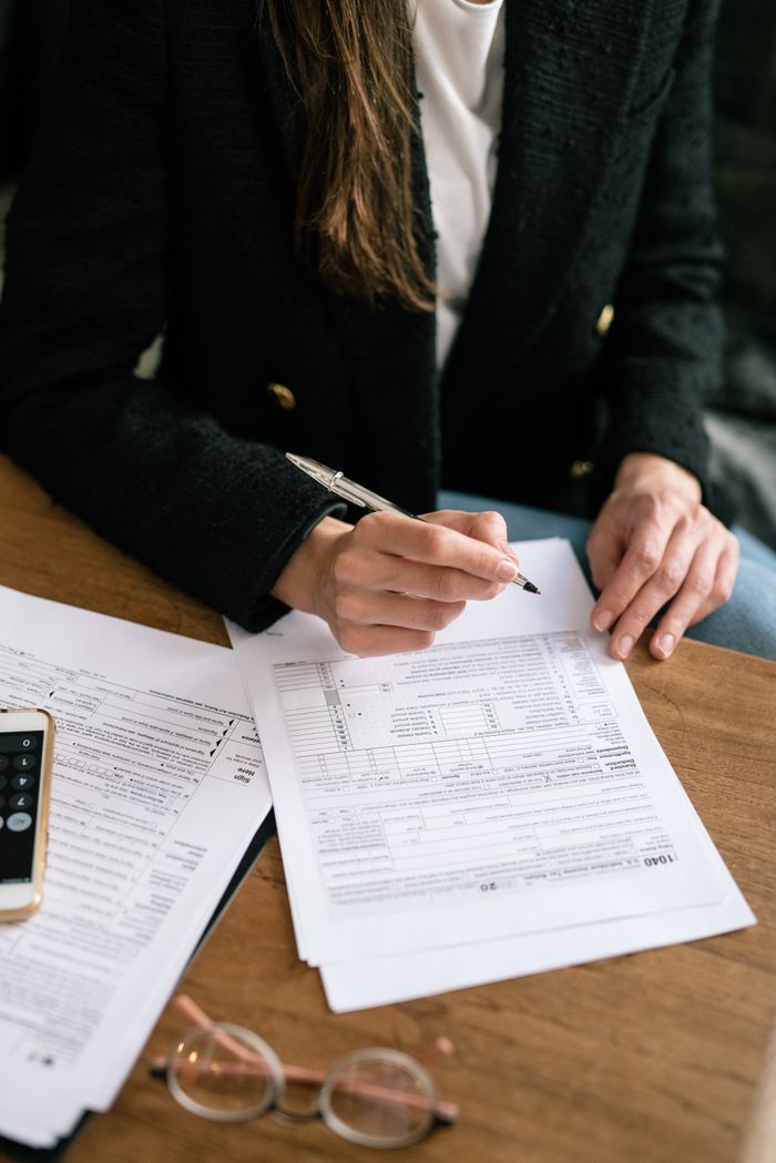 pexels photo 7247401 Close-up of a person reviewing and signing documents at a wooden desk, business attire.