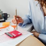 A woman is calculating expenses using a calculator and papers at her desk.
